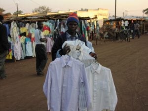 A Malawian man holding several shirts in a market